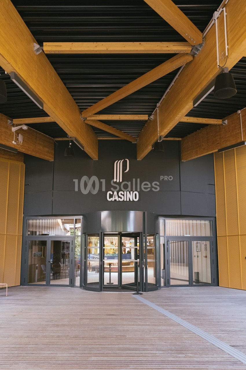 Entrée principale d'un casino moderne avec des structures en bois et un logo visible au-dessus des portes vitrées.