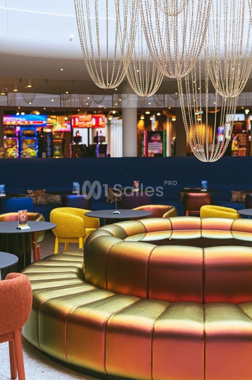 Banquettes circulaires colorées sous des lustres en chaînes, avec des jeux d'arcade en arrière-plan.