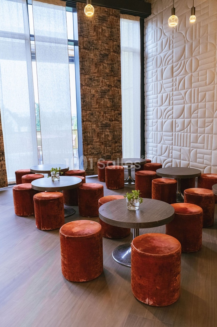 Salle moderne avec tables rondes, poufs en velours rouge et murs décorés de motifs géométriques en relief.