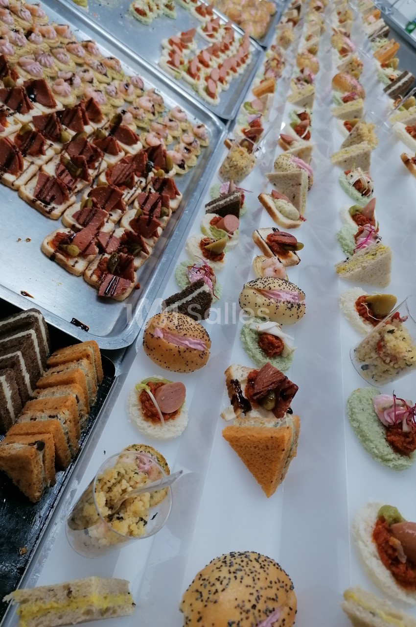 Plateaux de bouchées apéritives variées disposées en rangées sur une table, prêtes pour un service traiteur.