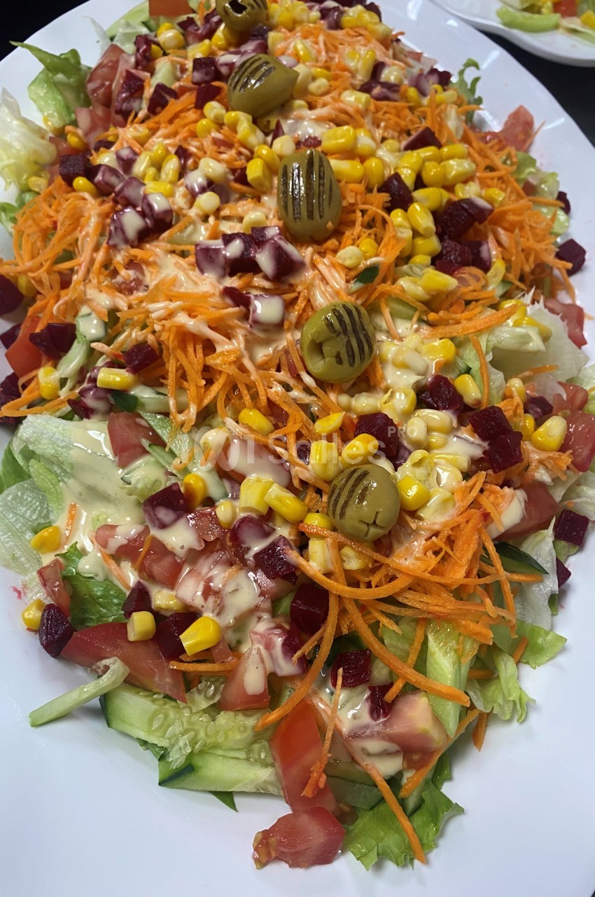 Assiette de salade composée avec laitue, tomates, carottes râpées, maïs, betteraves, olives et sauce.