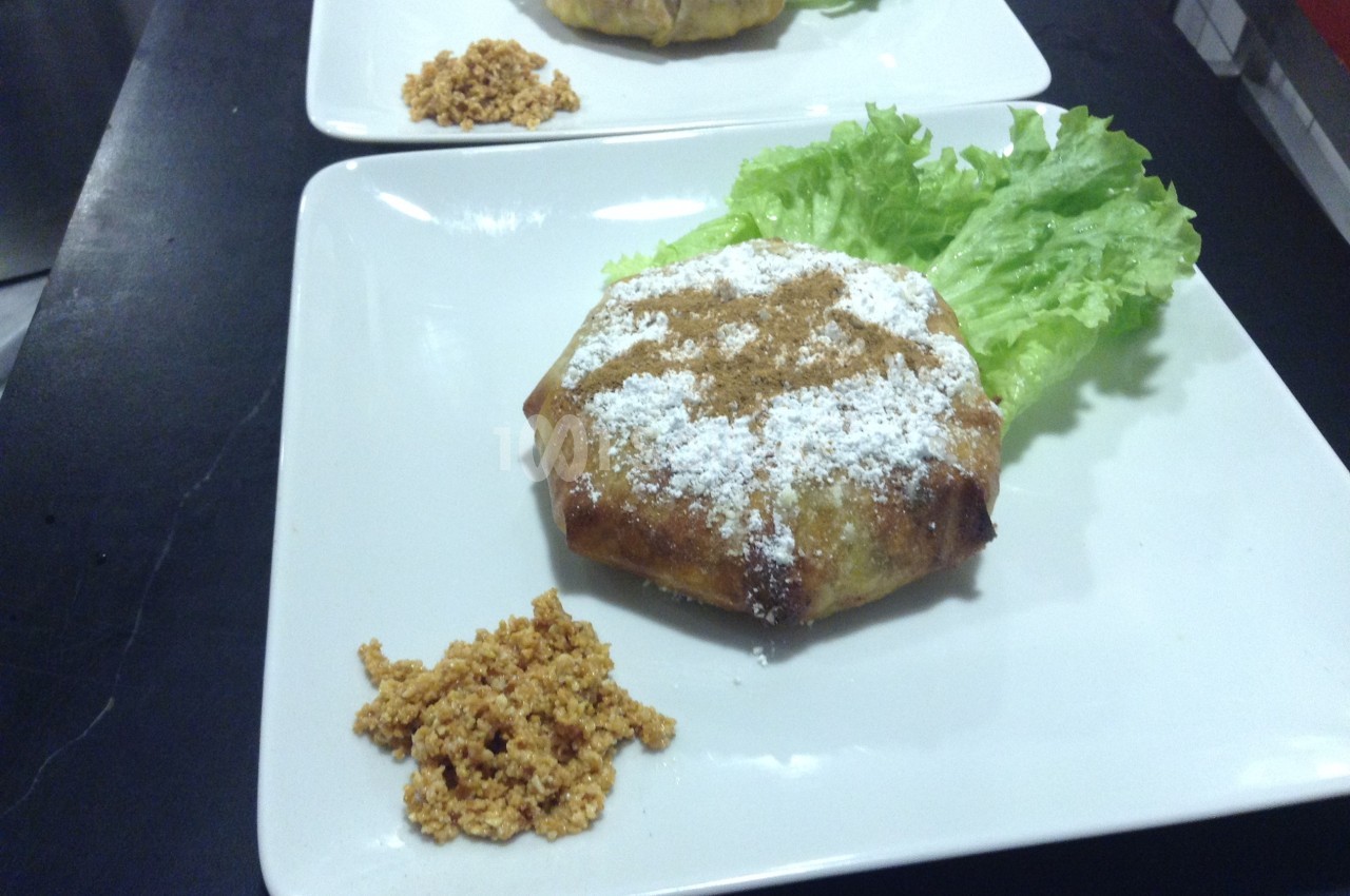 Plat de pastilla saupoudrée de sucre glace, servie avec une feuille de laitue et une garniture croustillante.