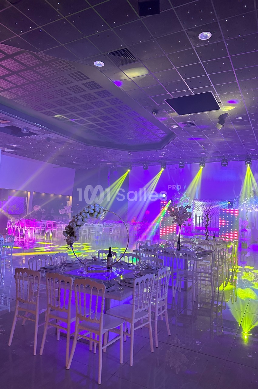 Salle de réception décorée avec des tables et des chaises, éclairée par des lumières colorées et des projecteurs.