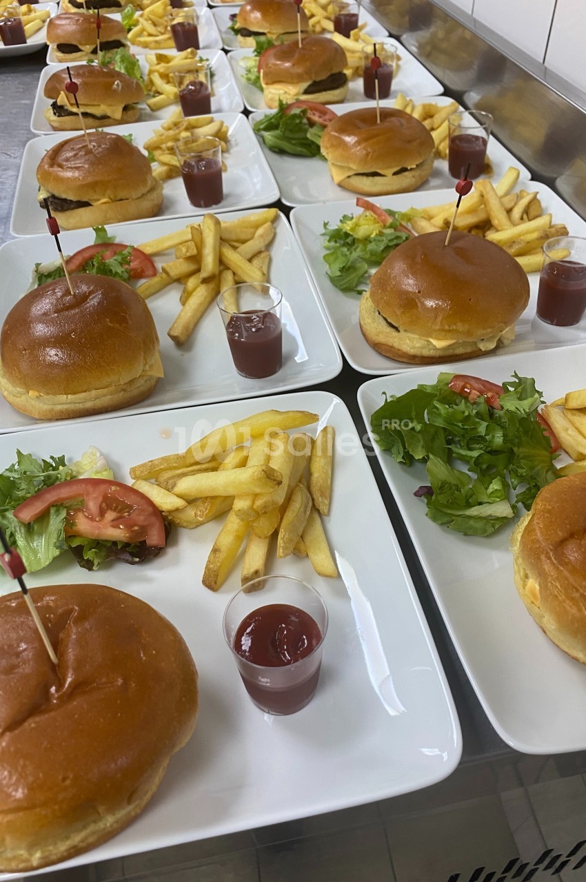 Assiettes alignées contenant des burgers, frites, salade et sauce ketchup, présentées sur un plan de travail.
