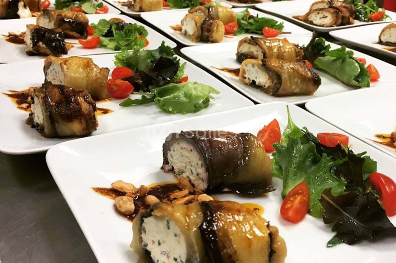 Assiettes dressées avec roulés d'aubergine farcis, salade verte, tomates cerises et sauce balsamique.