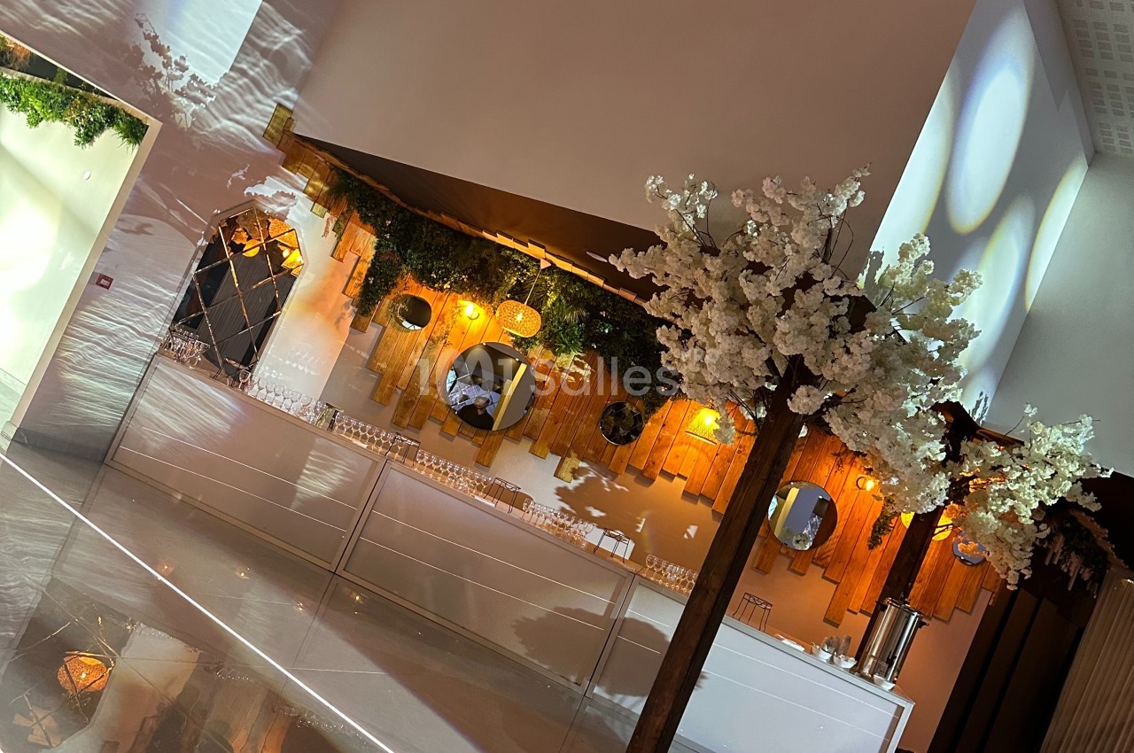 Décoration intérieure avec comptoir en bois, miroirs, guirlandes lumineuses et arbres artificiels ornés de fleurs blanches.
