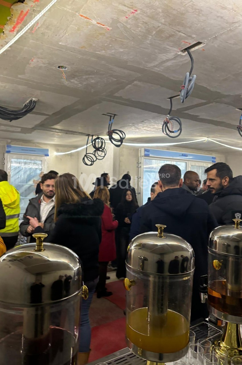 Groupe de personnes discutant dans un espace en construction, avec des distributeurs de boissons au premier plan.