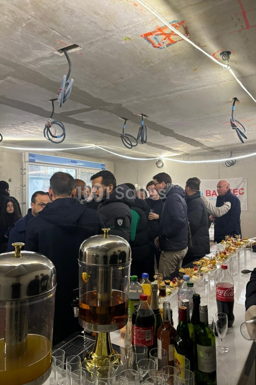 Groupe de personnes rassemblées dans un espace en construction, autour d'une table avec boissons et collations.