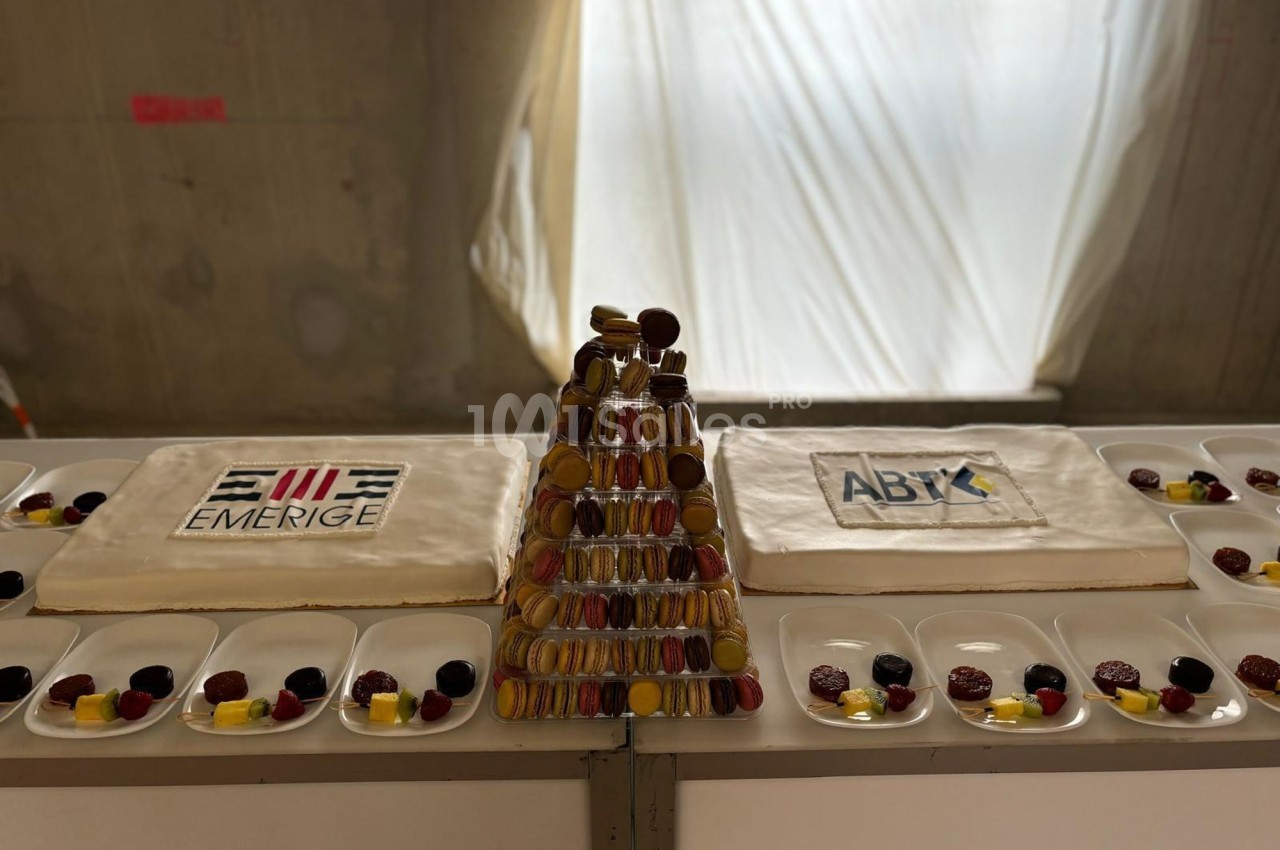 Deux gâteaux avec logos ’Emerige’ et ’ABT’ entourent une pyramide de macarons sur une table dressée.