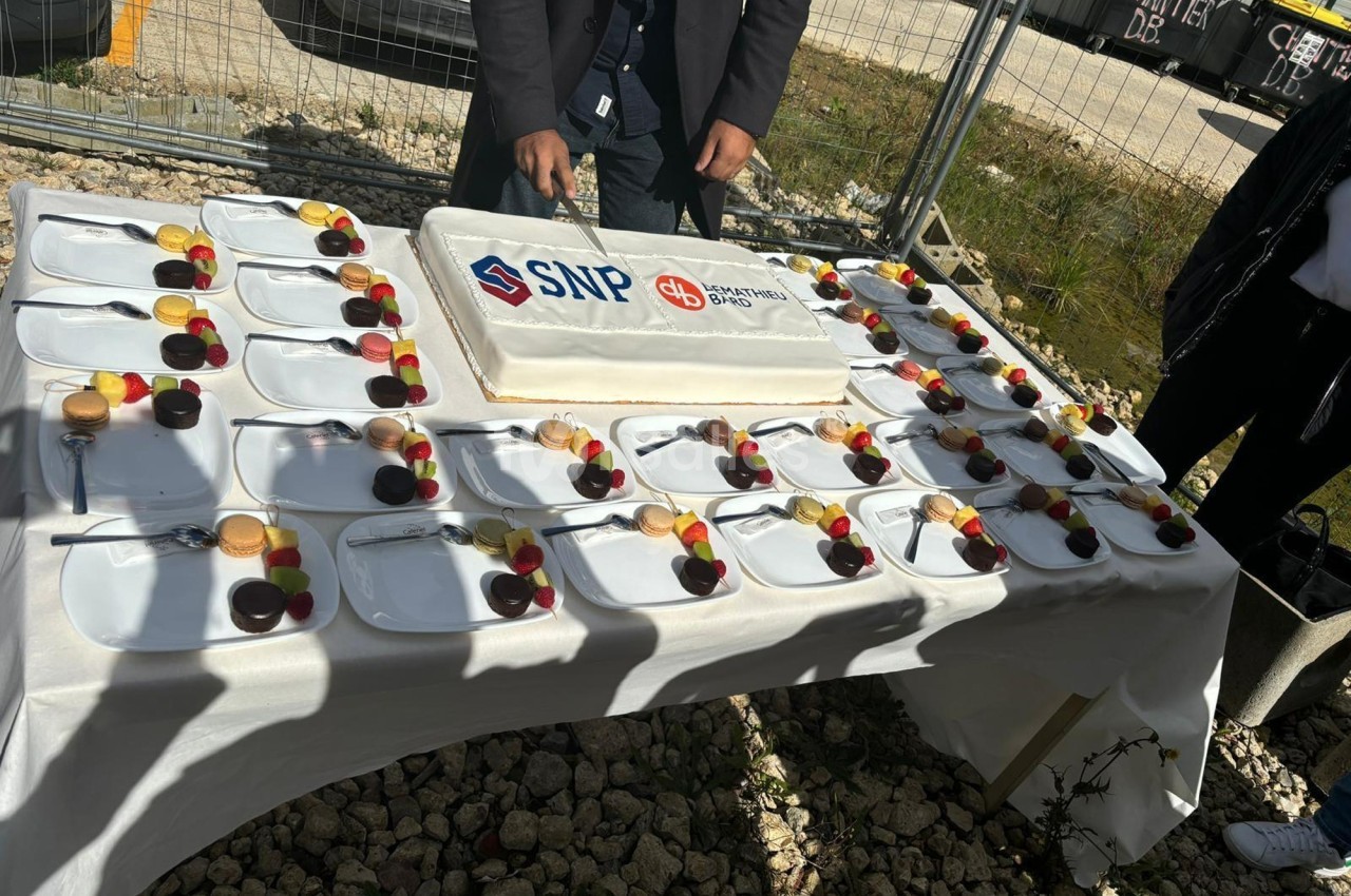 Un gâteau rectangulaire décoré de logos est découpé sur une table dressée avec des assiettes de desserts variés.