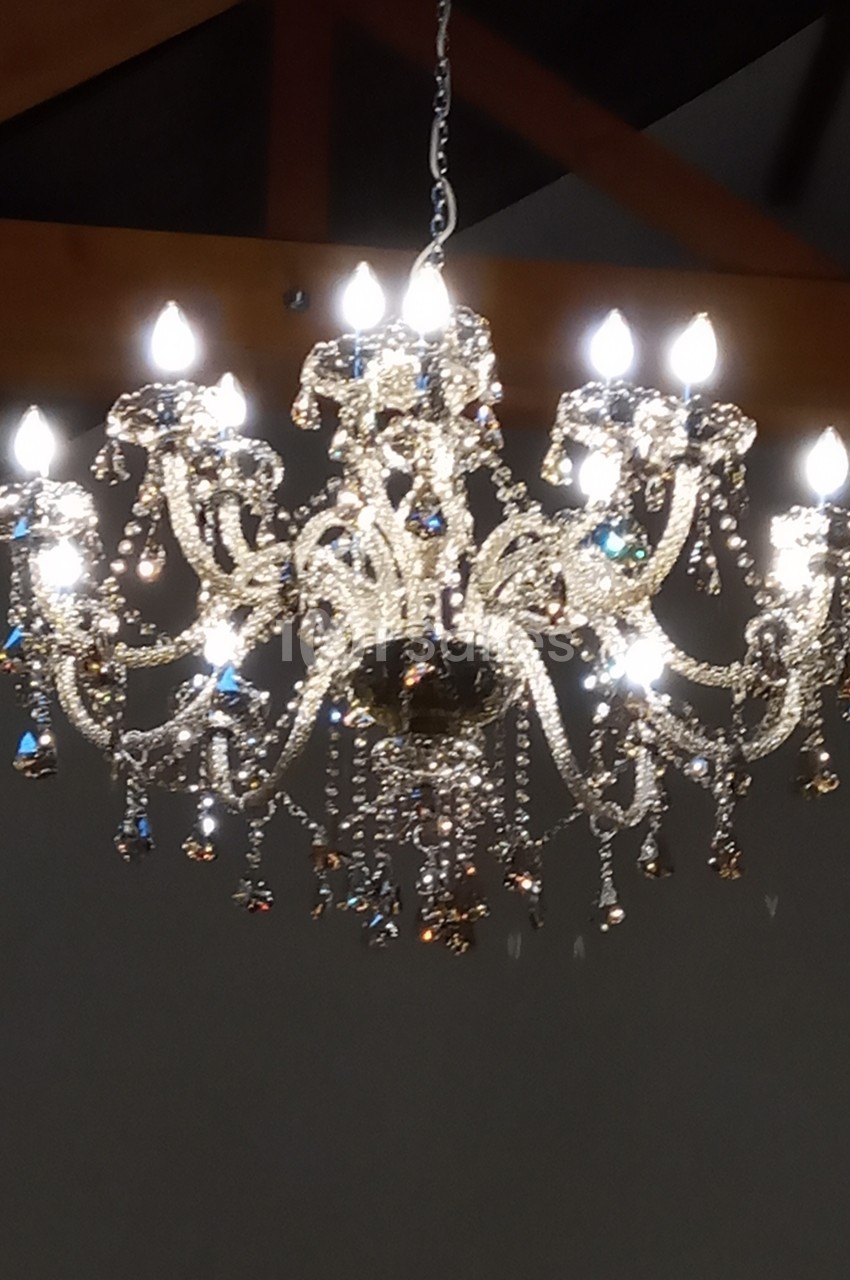 Lustre en cristal suspendu, éclairé avec des ampoules, reflétant la lumière dans un intérieur sombre.