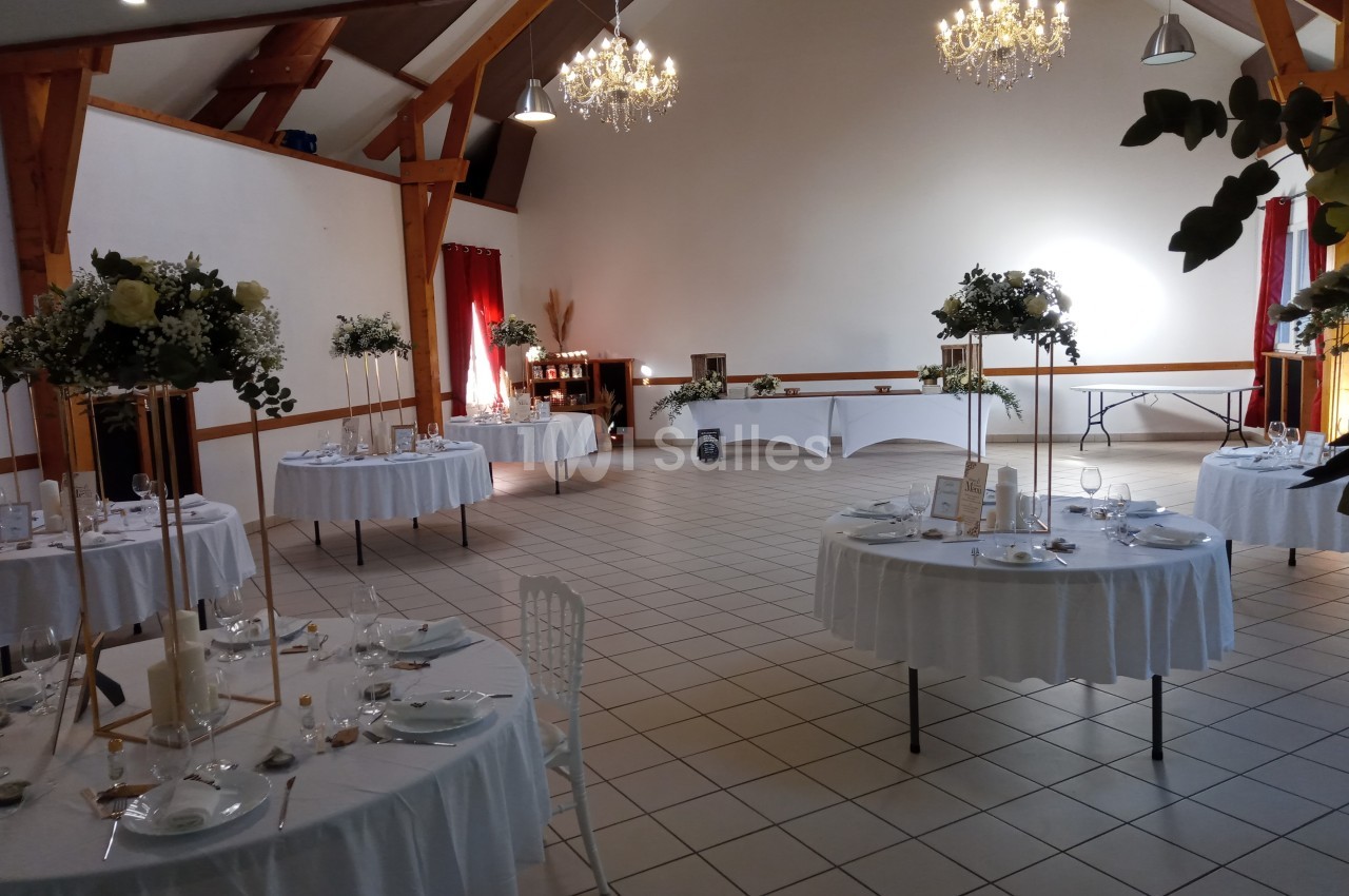Salle de réception décorée avec des tables rondes dressées, des chandeliers et des compositions florales.
