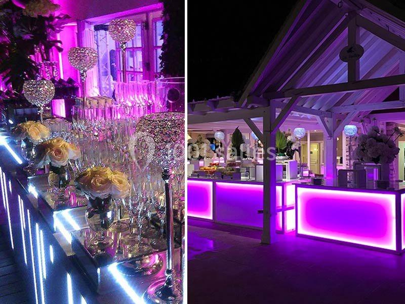 Comptoirs lumineux violets et décoration élégante avec verres, chandeliers et fleurs dans un cadre festif en soirée.