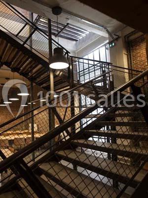 Escalier en métal avec rambardes en treillis dans un intérieur industriel éclairé par des lampes suspendues.