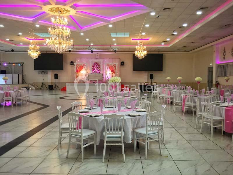 Salle de réception décorée avec des tables rondes, nappes blanches, chaises assorties et éclairage rose.