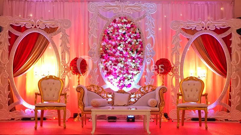 Décor de mariage avec canapé, fauteuils dorés, fleurs roses et éclairage chaleureux devant un fond orné.