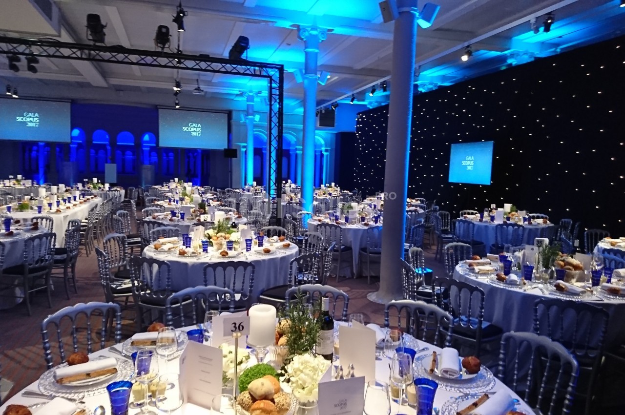 Salle de réception décorée pour un événement, avec tables dressées, éclairage bleu et écrans en arrière-plan.