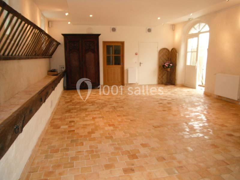 Salle lumineuse avec sol en carreaux de terre cuite, murs clairs, armoire en bois et porte-fenêtre vitrée.