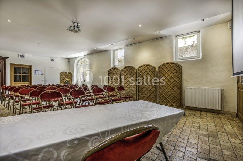 Salle de réunion avec chaises rouges alignées, table recouverte d'une nappe blanche et lumière naturelle provenant des…
