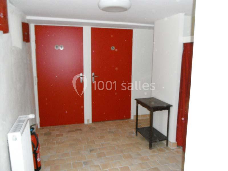 Deux portes rouges dans un couloir avec un sol en carrelage, une table noire et un extincteur au mur.