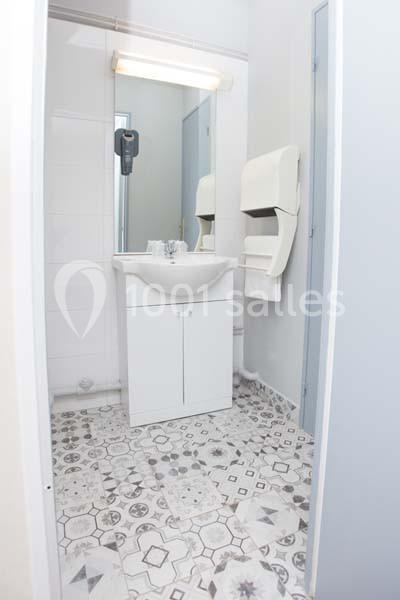 Lavabo blanc avec miroir éclairé, distributeur de papier et sol en carrelage à motifs géométriques.