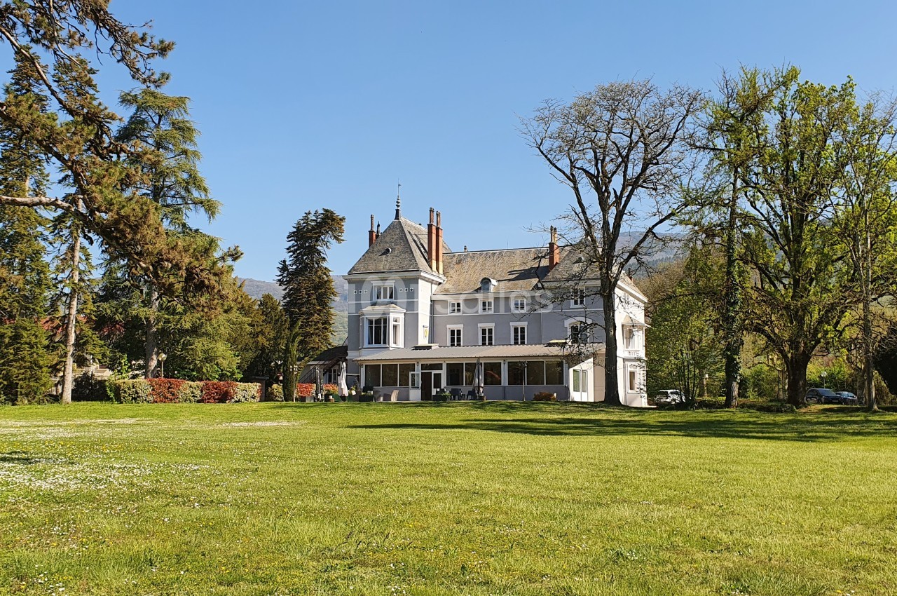 Grande maison de style classique entourée d'arbres et d'une pelouse verdoyante sous un ciel dégagé.