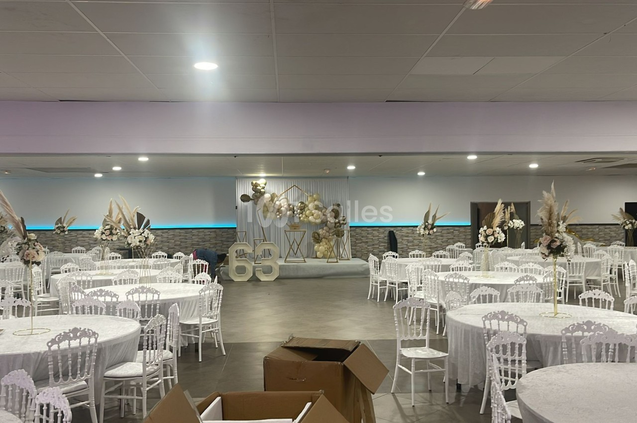 Salle de réception décorée avec des tables rondes, des chaises blanches et des arrangements floraux élégants.