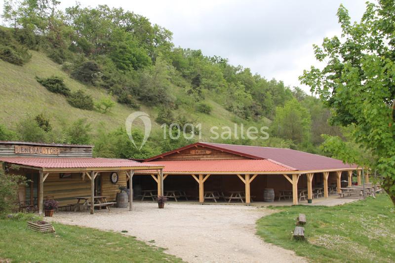 Abri en bois avec tables de pique-nique, situé dans un cadre naturel verdoyant au pied d'une colline.