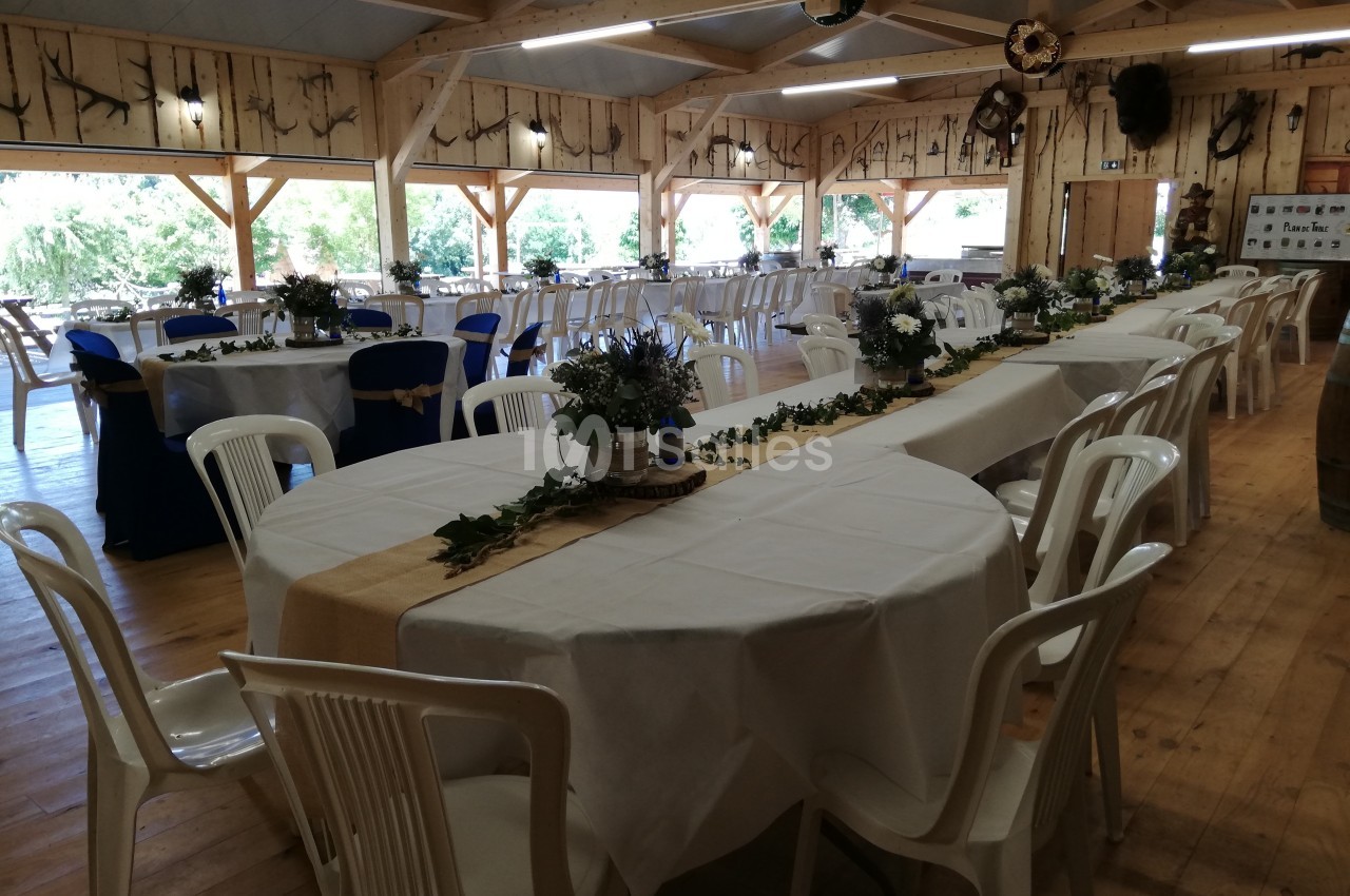 Salle de réception en bois décorée pour un événement, avec tables dressées, nappes blanches et arrangements floraux.