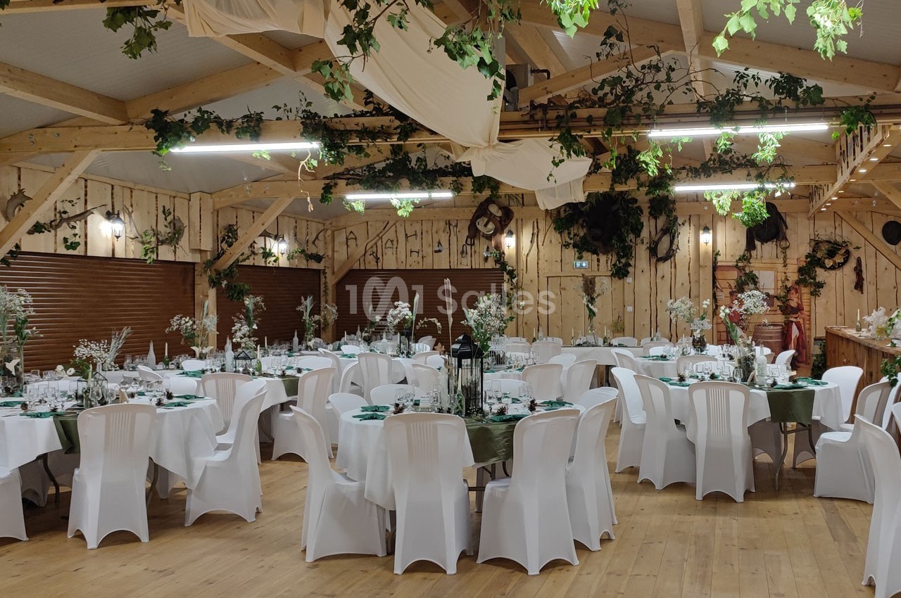 Salle de réception décorée avec des tables rondes, nappes blanches, chaises assorties et ornements végétaux suspendus.