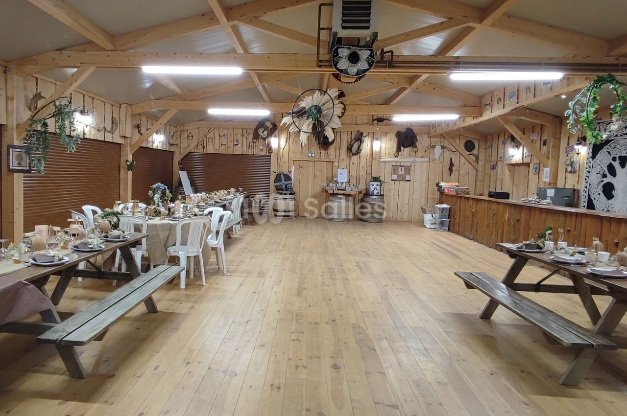 Salle en bois décorée dans un style rustique, avec tables dressées pour un repas et éléments de décoration champêtre.