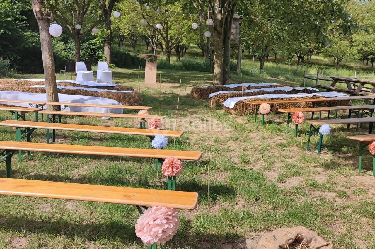 Disposition d'une cérémonie en plein air avec bancs en bois, bottes de paille décorées et allée centrale ornée de pompons…