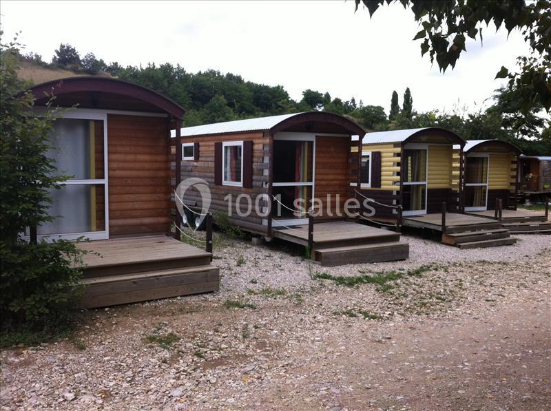 Quatre roulottes en bois alignées sur un terrain gravillonné, entourées de végétation et d'arbres.
