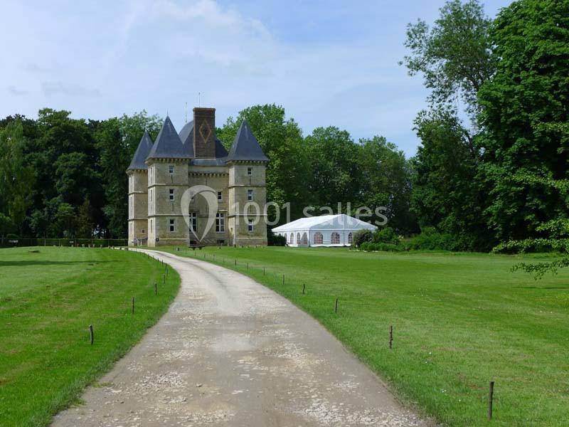 Allée gravillonnée menant à un château entouré de verdure avec une tente blanche sur la droite.