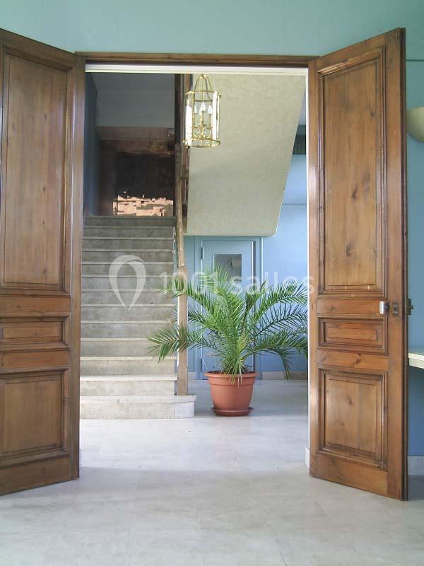 Vue d'une entrée avec des portes en bois ouvertes, un escalier en béton et une plante en pot au centre.