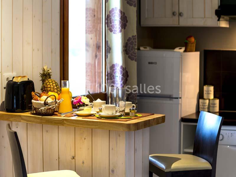 Petit-déjeuner servi sur un comptoir en bois dans une cuisine lumineuse avec réfrigérateur et décoration florale.