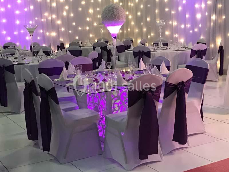 Salle de réception décorée avec des tables élégantes, des chaises blanches ornées de nœuds noirs et un éclairage tamisé.