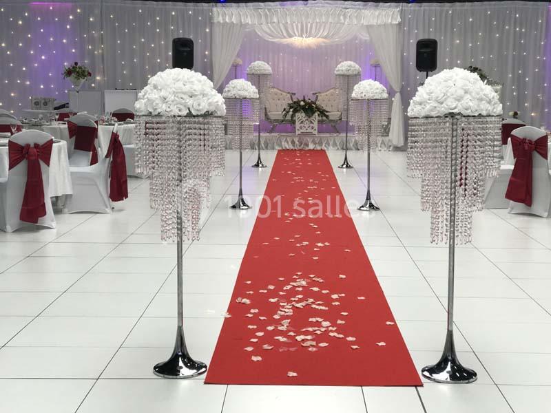 Allée centrale avec tapis rouge, décorée de colonnes ornées de fleurs blanches et cristaux, dans une salle de réception.