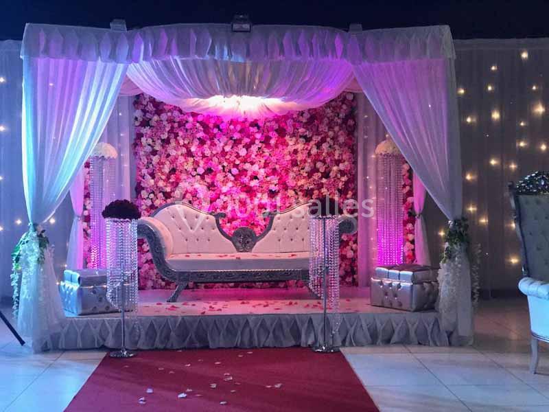 Décor de mariage avec canapé argenté, rideaux blancs, mur de fleurs roses et éclairage tamisé.