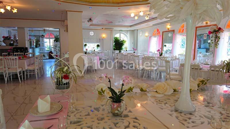 Salle de réception lumineuse avec tables dressées, décorations florales et grandes fenêtres laissant entrer la lumière…