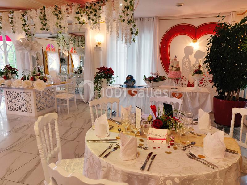 Salle de réception décorée pour un mariage avec tables dressées, fleurs, et ornements en forme de cœur.