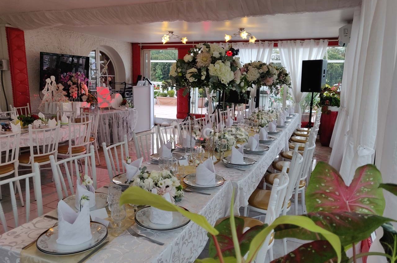 Salle décorée pour un événement avec une longue table dressée, ornée de fleurs blanches et de serviettes pliées.