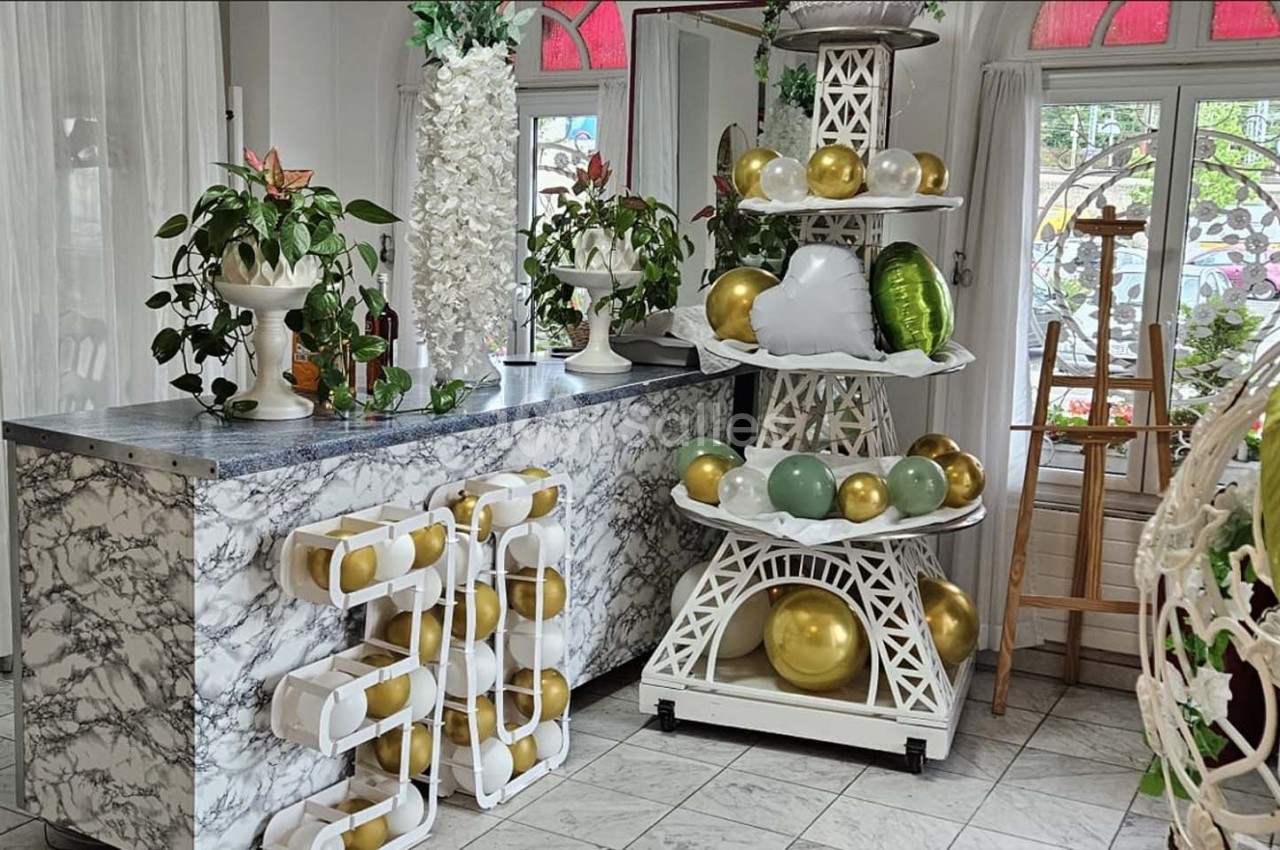 Décoration intérieure avec comptoir en marbre, plantes, ballons dorés et blancs disposés sur une structure décorative.