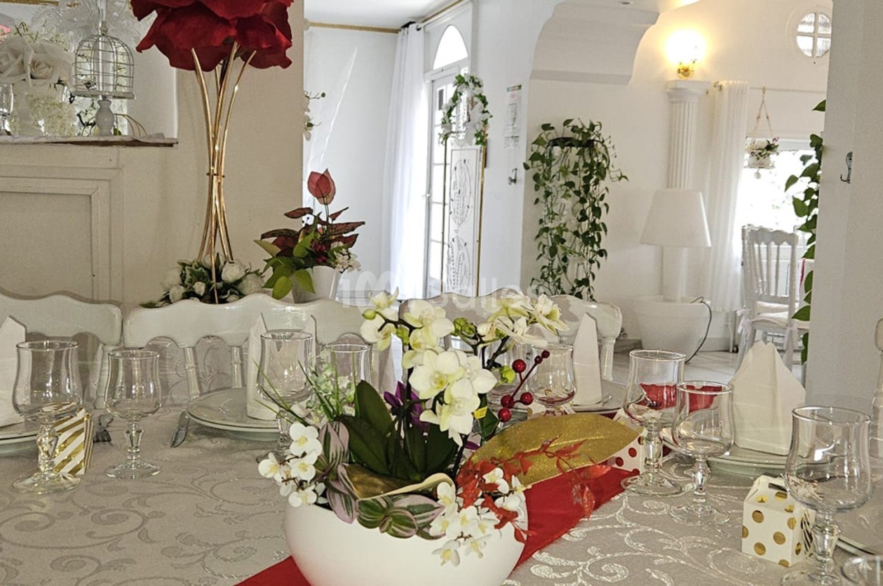 Table élégamment dressée avec nappe blanche, vaisselle raffinée et décoration florale dans une salle lumineuse.