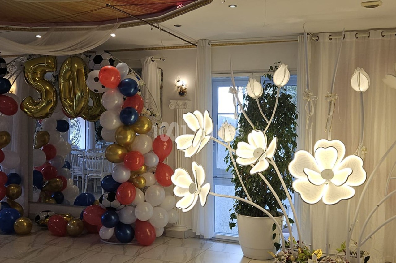 Décoration de salle avec arche de ballons colorés, chiffres ’50’ dorés et lampes en forme de fleurs lumineuses.