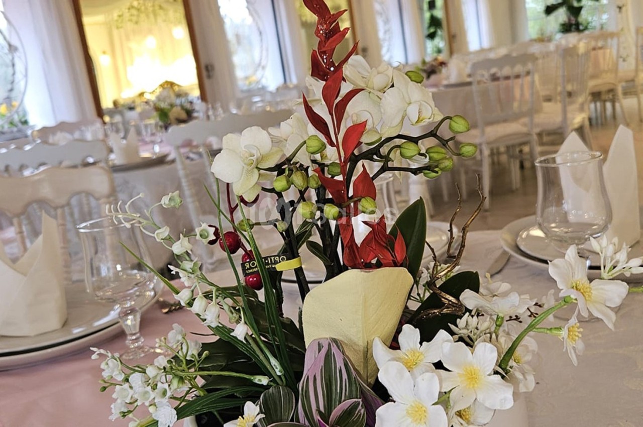 Centre de table floral avec des orchidées blanches et rouges, entouré de vaisselle sur une table de réception élégante.