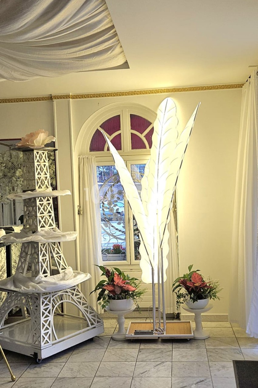 Lampadaire en forme de feuilles blanches éclairé, entouré de plantes et d'une décoration en forme de tour Eiffel blanche.