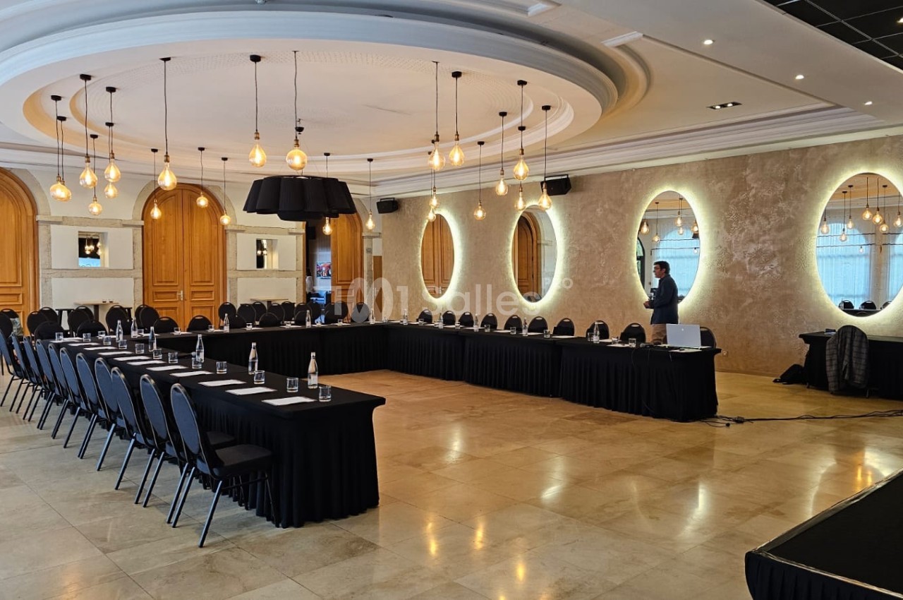 Salle de conférence élégante avec tables en U, chaises noires, éclairage suspendu et miroirs décoratifs sur les murs.