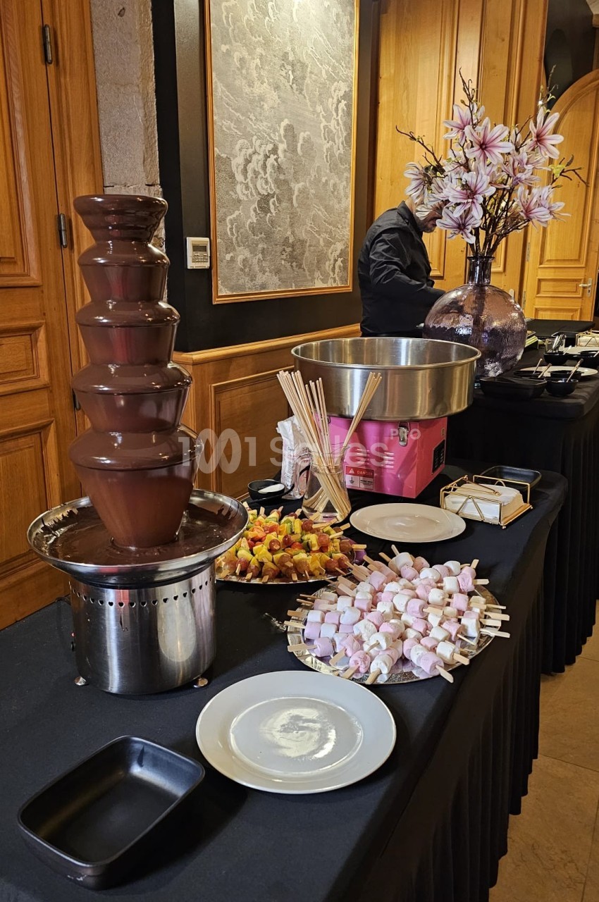 Fontaine de chocolat avec brochettes de fruits et guimauves disposées sur une table de buffet élégante.