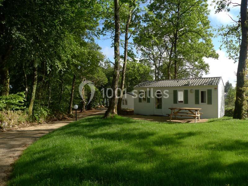 Mobil-home blanc entouré d'arbres, avec une table de pique-nique en bois sur une pelouse verte.